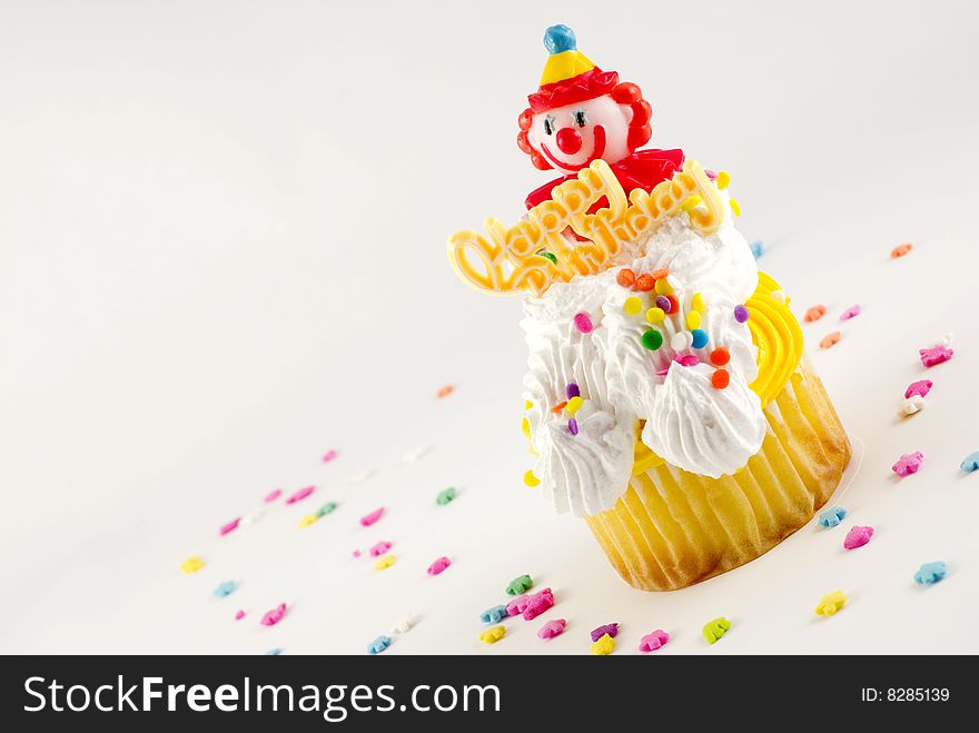 Happy Birthday Clown Cupcake diagonal in corner with plastic clown and Happy Birthday decoration white background with sprinkles and copy space