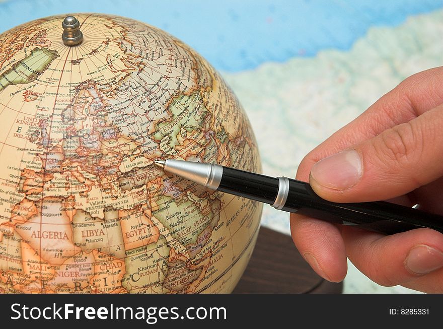A hand holds the pen and indicates on the globe. A hand holds the pen and indicates on the globe