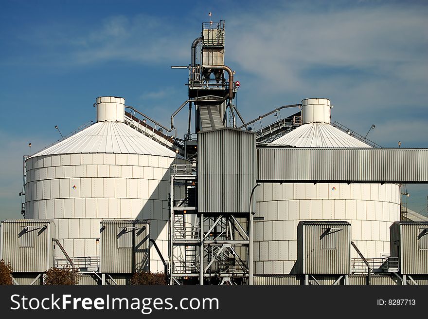 Two large tanks and conveyor belt at an oil refinery in an industrial neighborhood. Two large tanks and conveyor belt at an oil refinery in an industrial neighborhood.