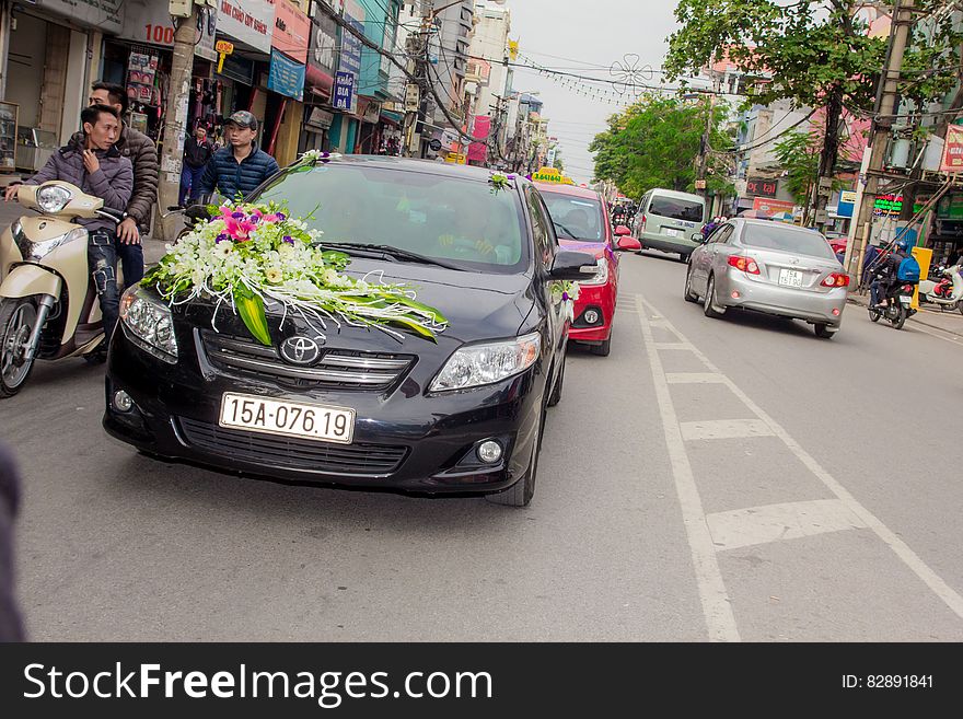 Flowers on hood of car driving down urban street.