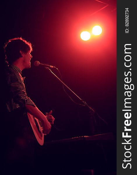 Singer playing acoustic guitar while performing onstage in spotlight. Singer playing acoustic guitar while performing onstage in spotlight.
