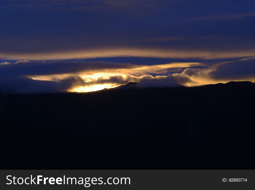 Sun setting through clouds in blue skies over landscape. Sun setting through clouds in blue skies over landscape.