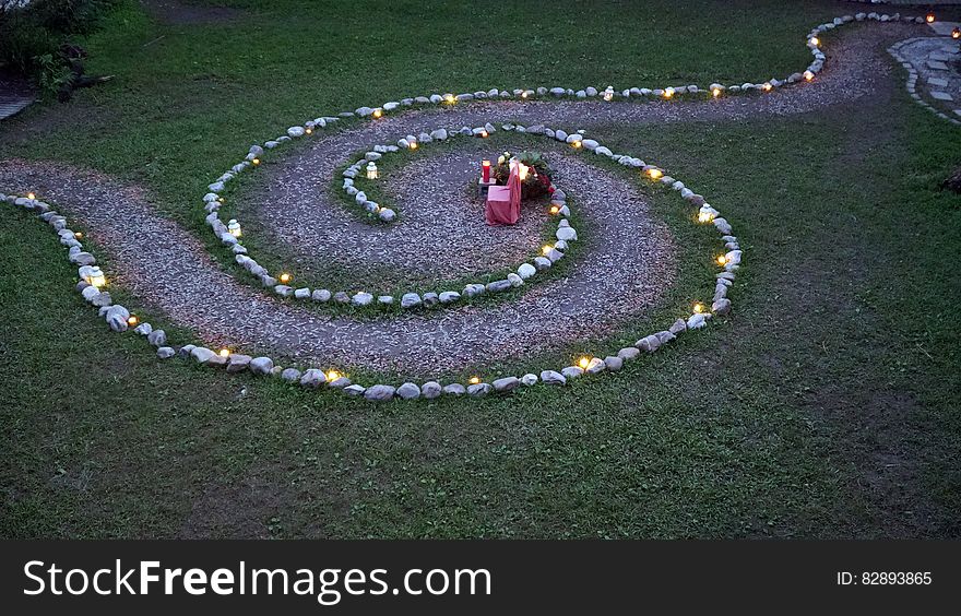 A garden path in the shape of a spiral with lanterns on the sides and a chair in the middle. A garden path in the shape of a spiral with lanterns on the sides and a chair in the middle.