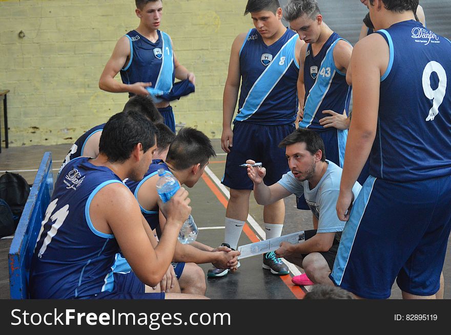 Group of players on a basketball court listening to their coach give a team talk. Group of players on a basketball court listening to their coach give a team talk.