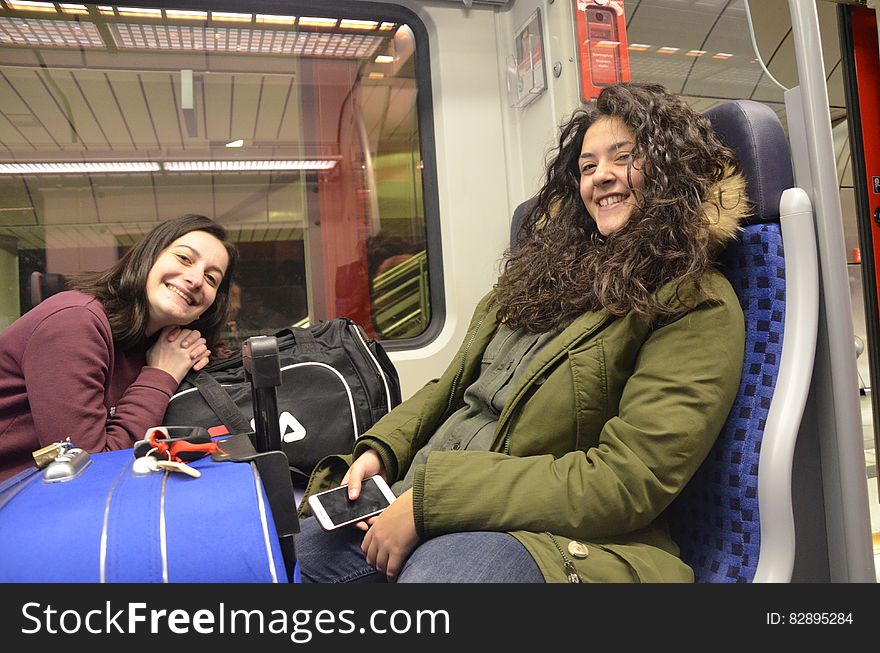 Happy smiling girls, maybe teenagers, on a train surrounded by luggage glad to be coming home or setting off for a holiday, background train interior. Happy smiling girls, maybe teenagers, on a train surrounded by luggage glad to be coming home or setting off for a holiday, background train interior.