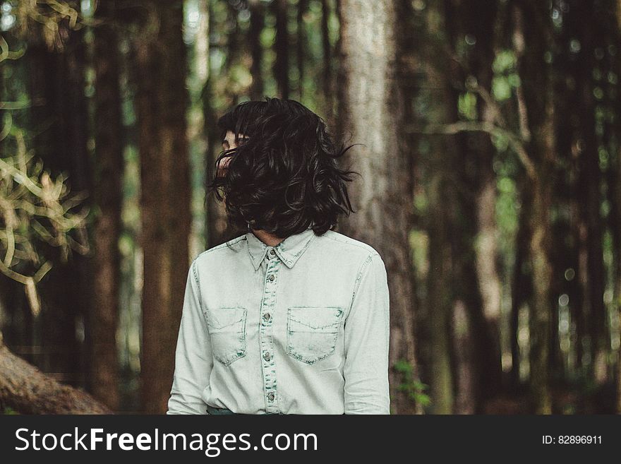 Mysterious woman wearing smart pale green shirt, head with shock of black hair turned sideways with thick forest in the background. Mysterious woman wearing smart pale green shirt, head with shock of black hair turned sideways with thick forest in the background.