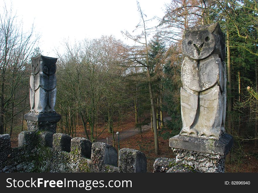 Owl sculpture on old building with forest in background.