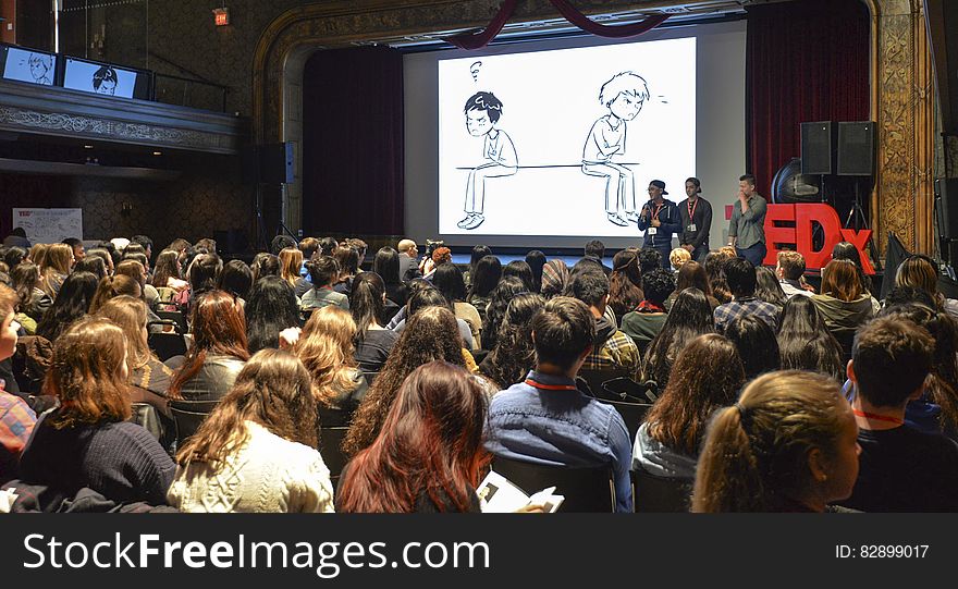 Speakers onstage in crowded hall during 2016 TEDx conference.