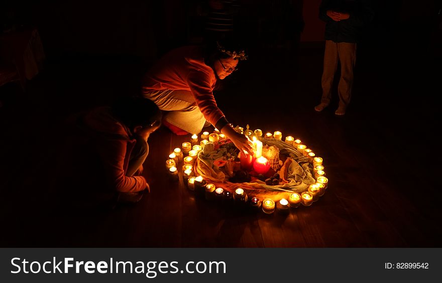 A circle of burning candles and a few people around it, a woman putting one in the middle.