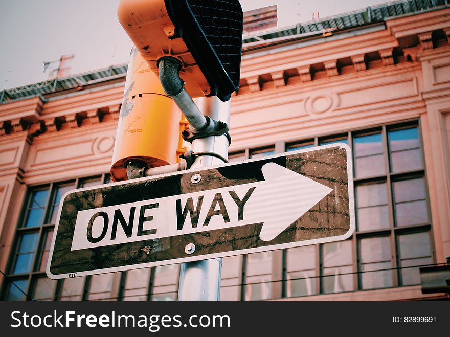 One way road sign on traffic light pole on sunny day.