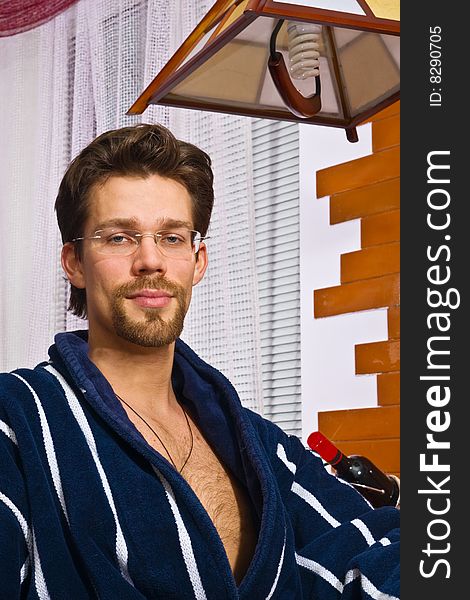 Young man wearing blue striped bathrobe sitting in his kitchen and smiling. Young man wearing blue striped bathrobe sitting in his kitchen and smiling