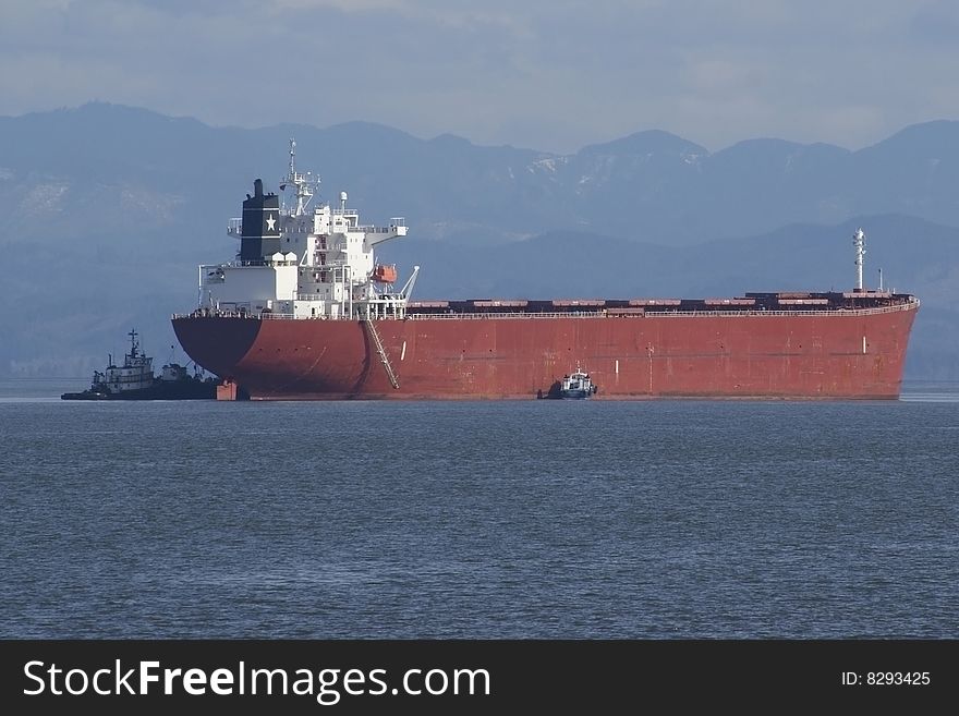 A cargo ship arrives with the assistance of tug boats. A cargo ship arrives with the assistance of tug boats.