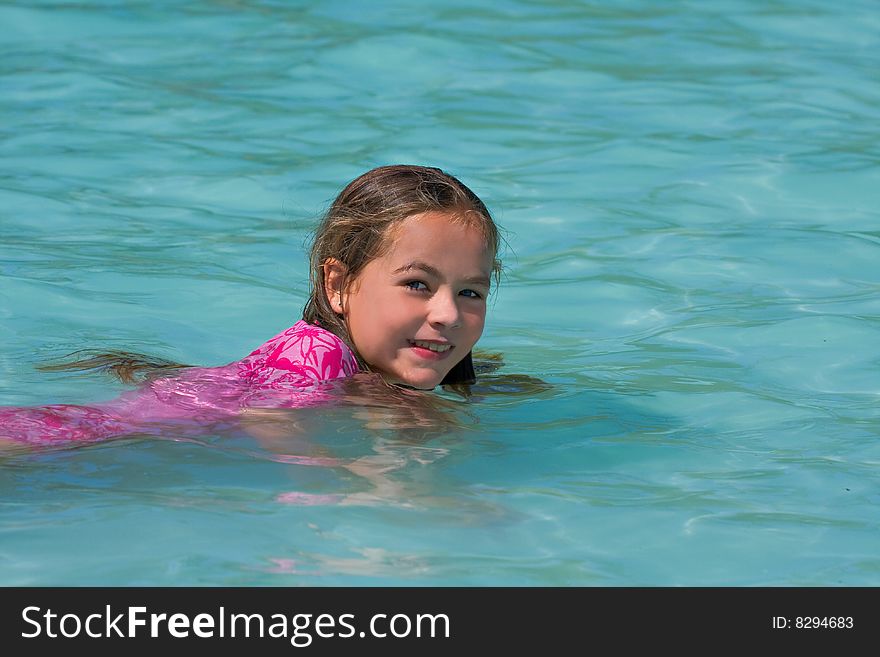 Young girl swimming in a pool looking at the camera with a smile. Young girl swimming in a pool looking at the camera with a smile