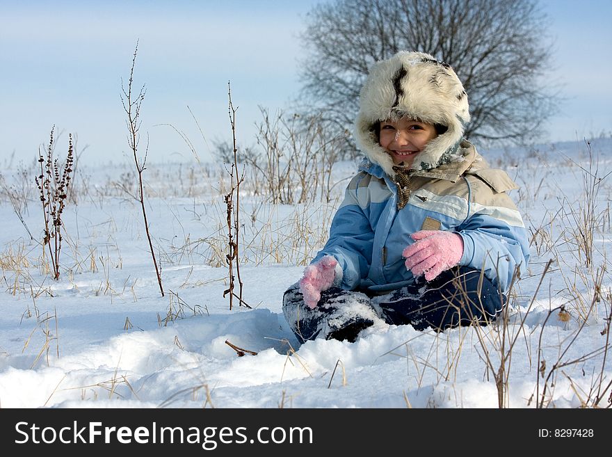 Cute girl in the fur-cap sitting in snow