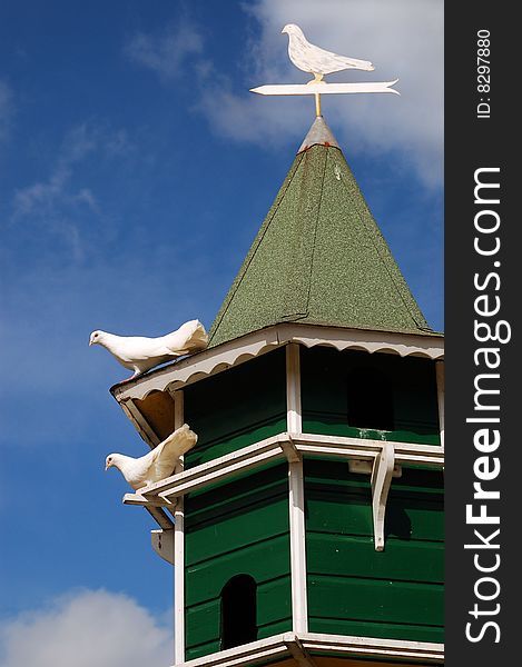 Two white pigeons are on the roof of wind vane.