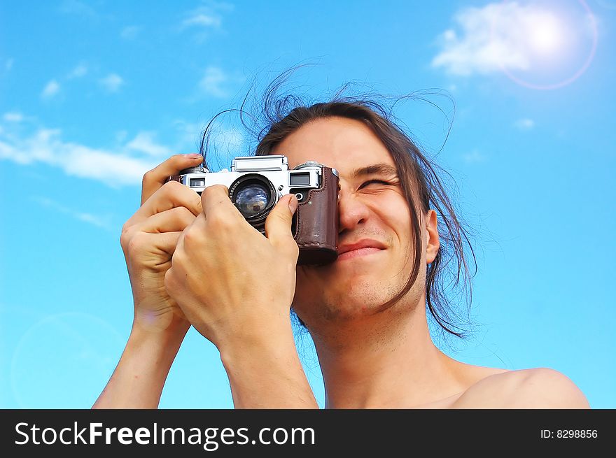 Young man holding old camera, focusing the image, against blue sky. Young man holding old camera, focusing the image, against blue sky