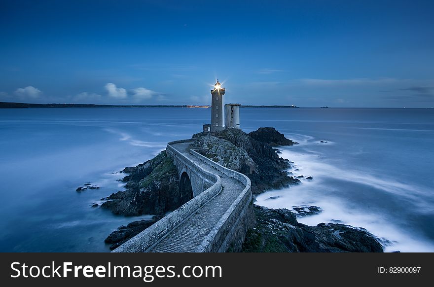 Exterior of lighthouse at end of winding path along rocky coastline illuminated at twilight. Exterior of lighthouse at end of winding path along rocky coastline illuminated at twilight.