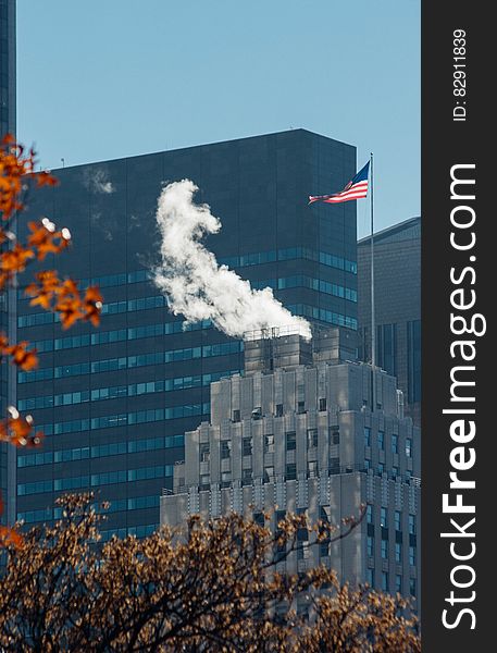 Steam coming from rooftop of modern building in city skyline with American flag. Steam coming from rooftop of modern building in city skyline with American flag.