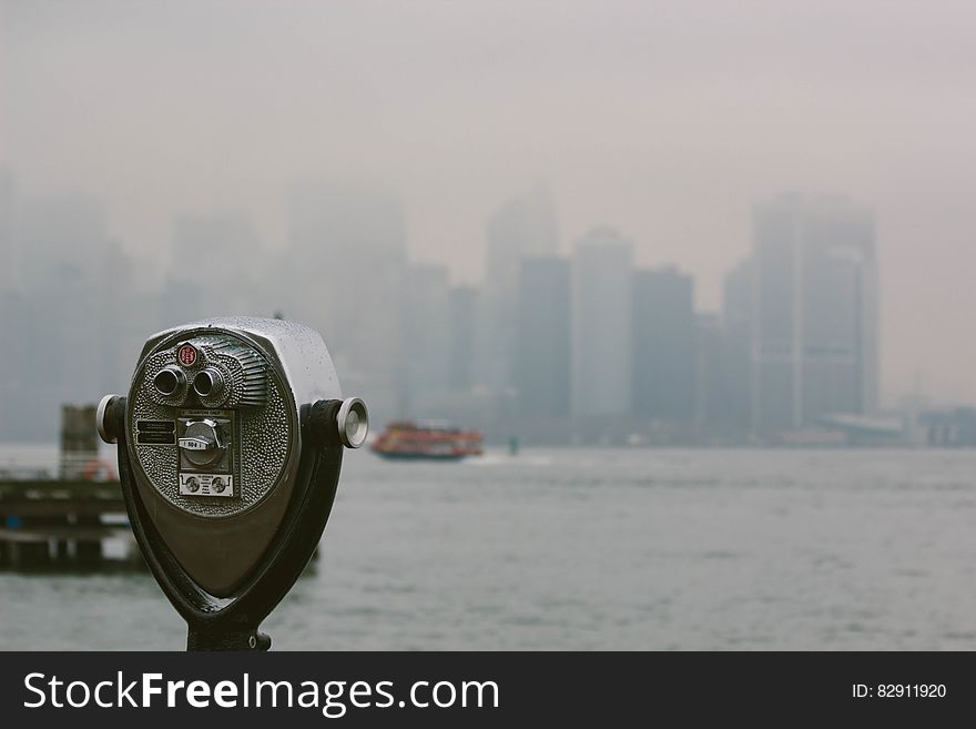 Public binocular style telescope looking over river with New York city skyline in background, USA. Public binocular style telescope looking over river with New York city skyline in background, USA.