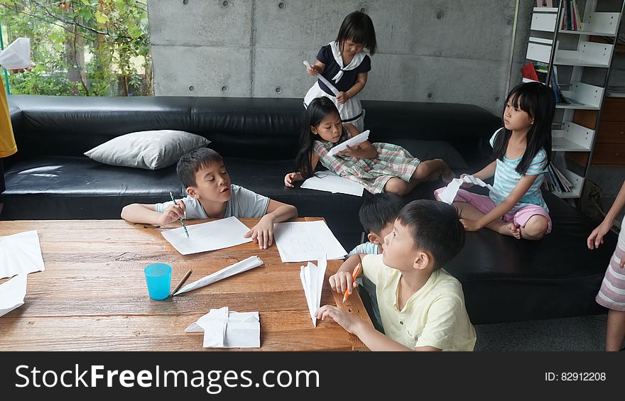 Group of children making paper airplanes on sofa inside home.