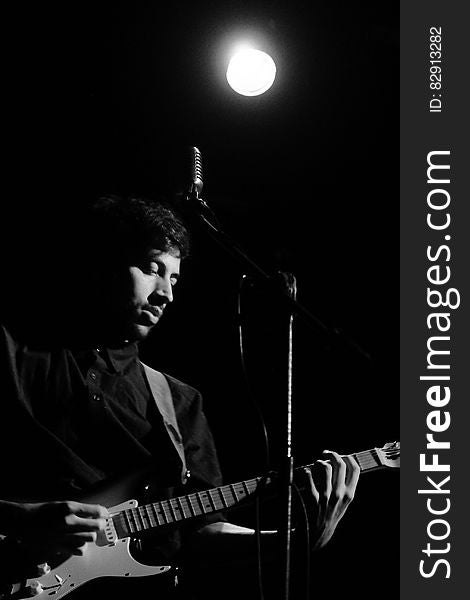 Musician playing guitar in front of microphone onstage in black and white with spotlight. Musician playing guitar in front of microphone onstage in black and white with spotlight.