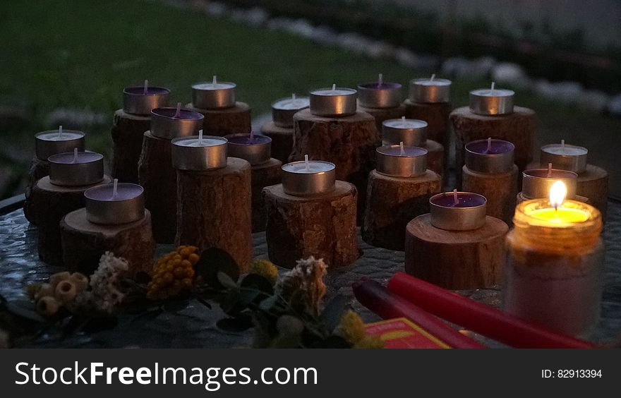 One lit and many unlit candles on outdoor display in evening.