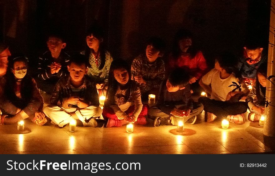 Children sitting on floor indoors illuminated by candlelight. Children sitting on floor indoors illuminated by candlelight.