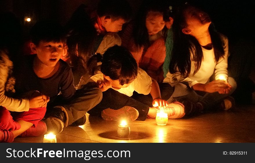 Children sitting on floor in candlelight during ceremony. Children sitting on floor in candlelight during ceremony.