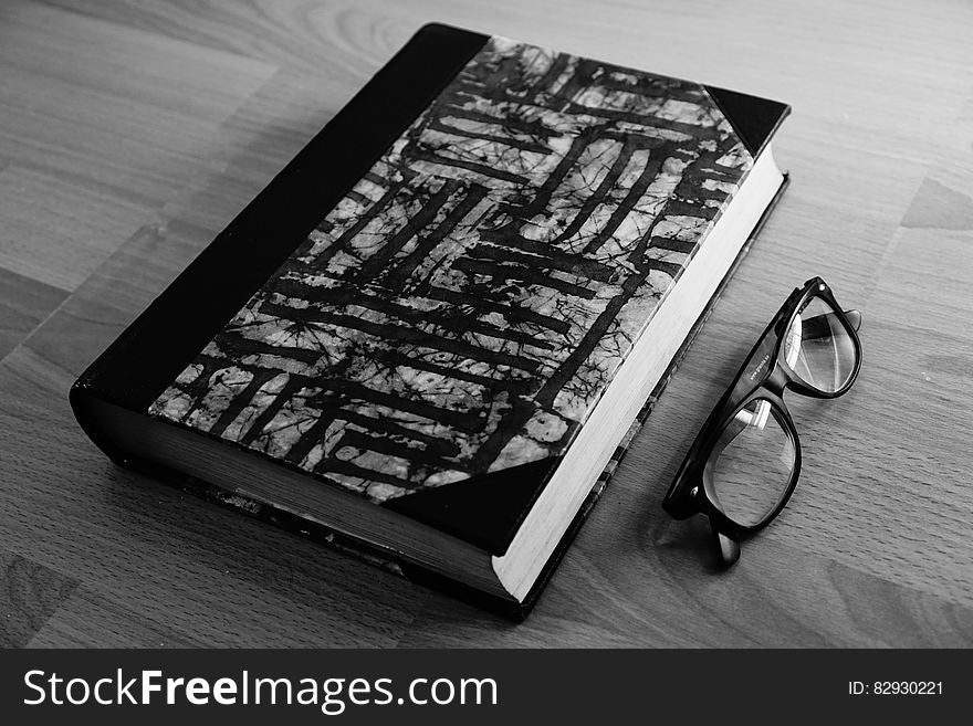 Grayscale Photo of Eyeglasses Near Thickbound Book