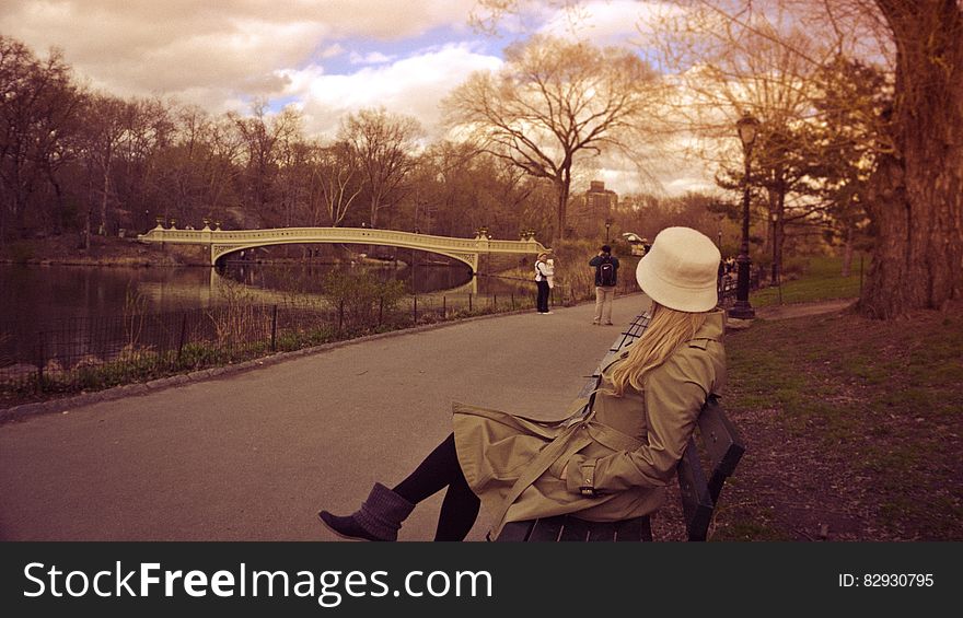 Woman in White Bucket Hat, Brown Coat and Boots Sitting on Bench at Park