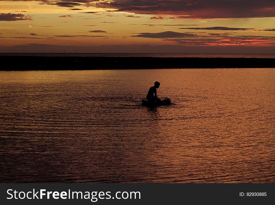 Silhouette Of Person On Body Of Water During Sunset