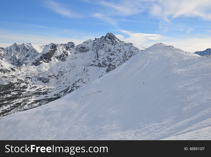 Alpine hikers from a distance climbing snow covered peak on sunny day. Alpine hikers from a distance climbing snow covered peak on sunny day.