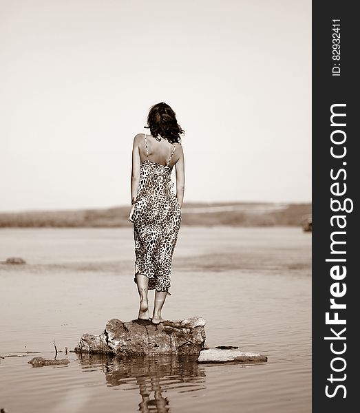 Woman Wearing Leopard Print Dress Standing On Stone On Body Of Water