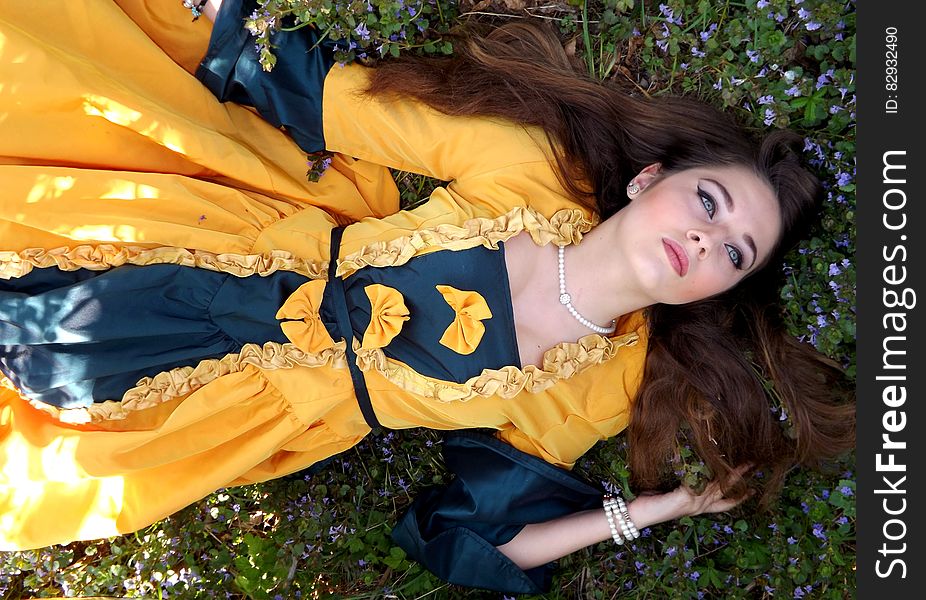 Woman in Yellow and Blue Dress Lying on a Grass Field