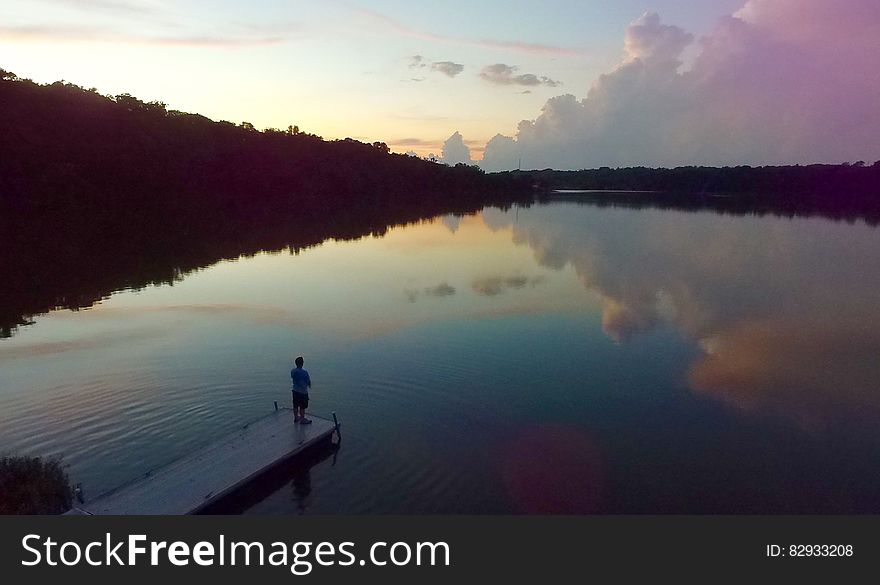 Man Standing on River Dock during Sunset
