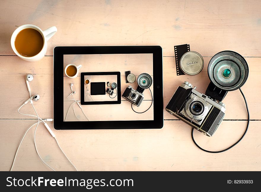 Still life of vintage film camera and tablet on wooden desktop with cup of coffee. Still life of vintage film camera and tablet on wooden desktop with cup of coffee.