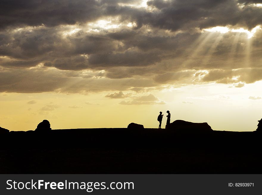 Silhouette of couple standing close together on rocks beside the sea with sunlight streaming through the clouds. Silhouette of couple standing close together on rocks beside the sea with sunlight streaming through the clouds.