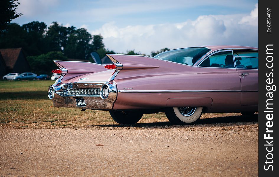 Rear of a pink classic automobile with tail-fins in countryside car park.