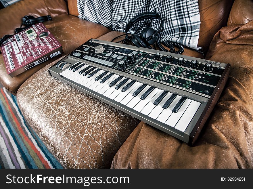 A keyboard synthesizer and a mixer on a vintage leather couch. A keyboard synthesizer and a mixer on a vintage leather couch.
