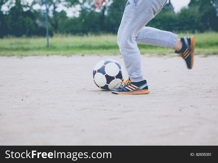 Person Kicking Soccer Ball on Gray Sand