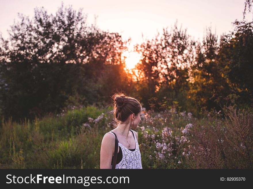 Selective Focus Photography of Woman Standing in the Middle of Grasses and Flowers during Golden Hour