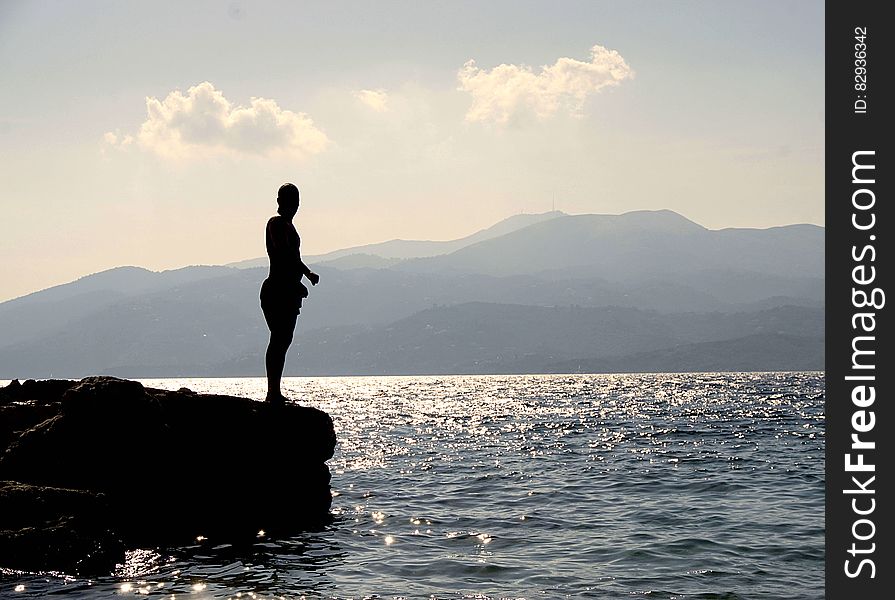 Person Standing On Rock Besides Sea Near Island During Daytime