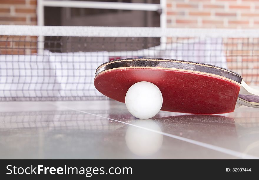 White Pingpong Ball Beneath Red Table Tennis Paddle