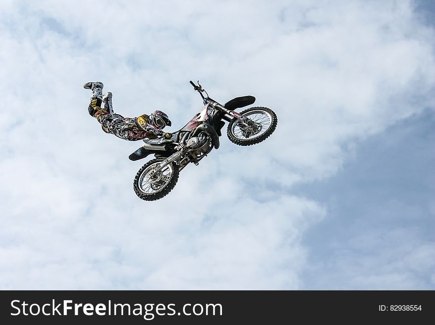 Motorbike stunt man flying through the air on a bike clinging only to the saddle, blue sky and cloud.