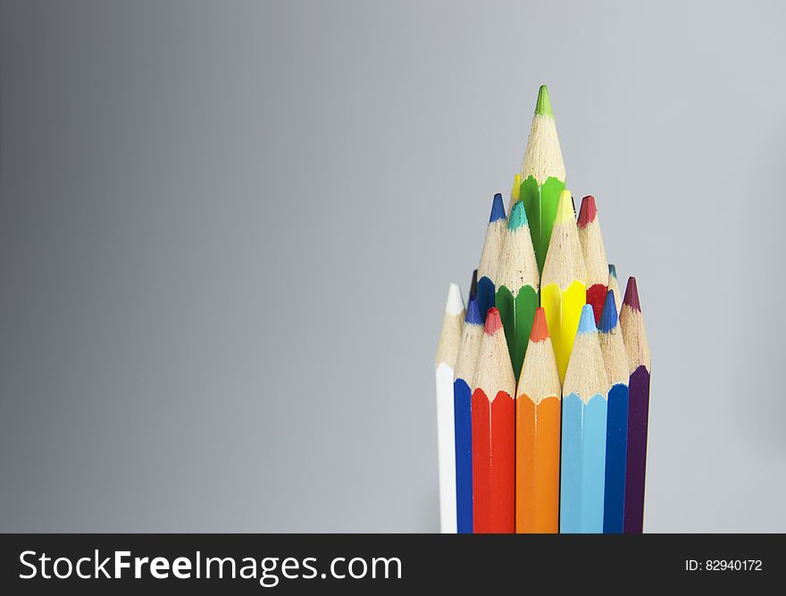 A bunch of color pencils forming a bigger pencil on gray background.