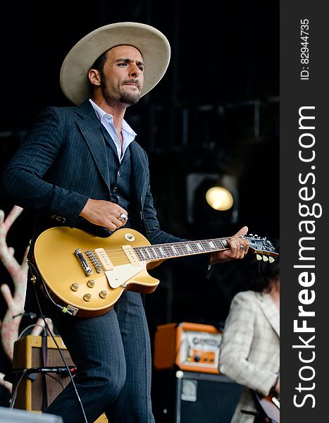 Man in Black and White Pinstripe Formal Coat and Pants Wearing Beige Hat Holding Brown Electric Guitar