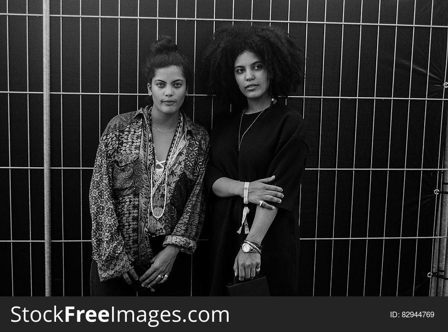 Greyscale Photo Of 2 Woman Standing Behind Steel Bars