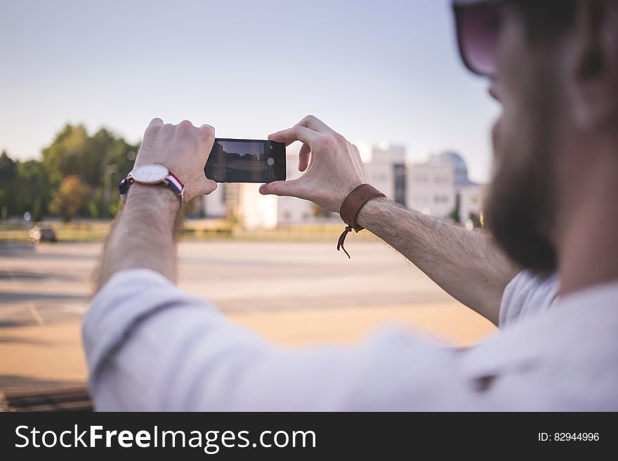 Tilt Shift Photo of Man Holding Black Smartphone Taking Photo of Gray Ground at Daytime