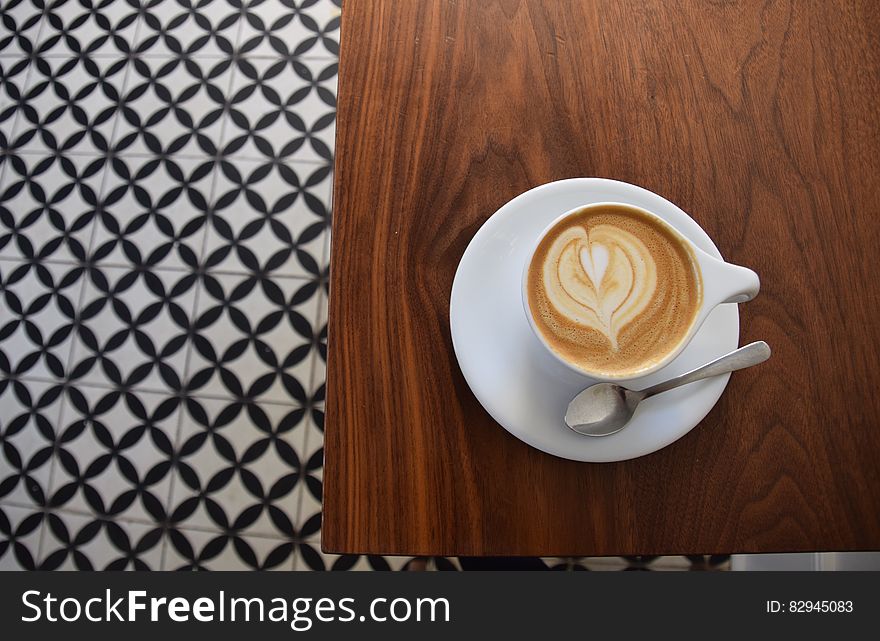 Overhead view of cup of cappuccino coffee on wooden table with decorative pattern.