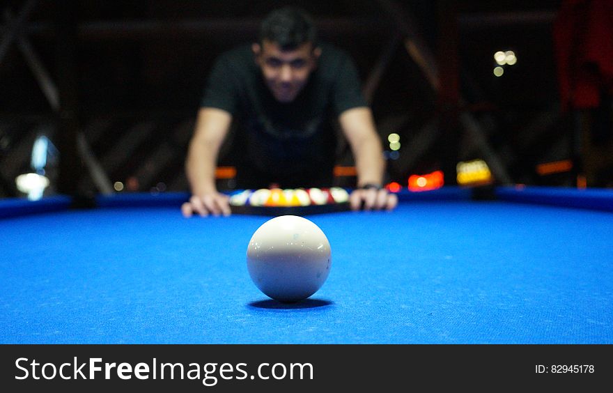 Man using a triangle to set up pool balls on blue baize table with white ball on foreground. Man using a triangle to set up pool balls on blue baize table with white ball on foreground.